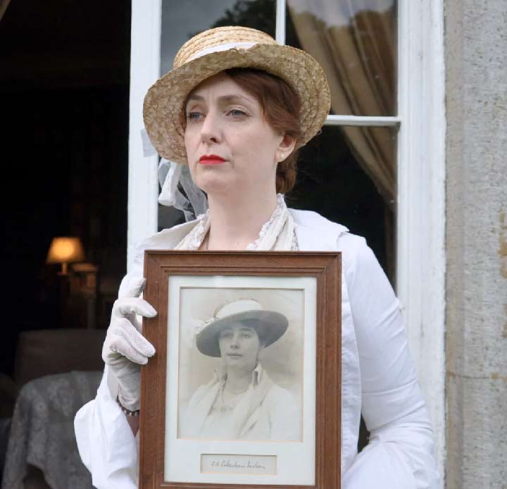 A woman in period dress holding an old photo.